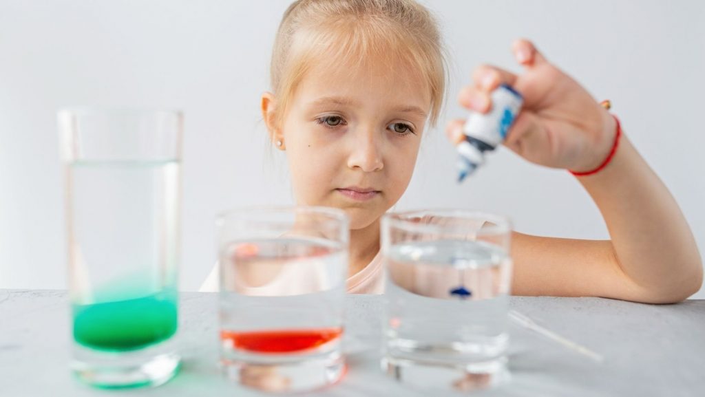 girl putting food color in water glasses